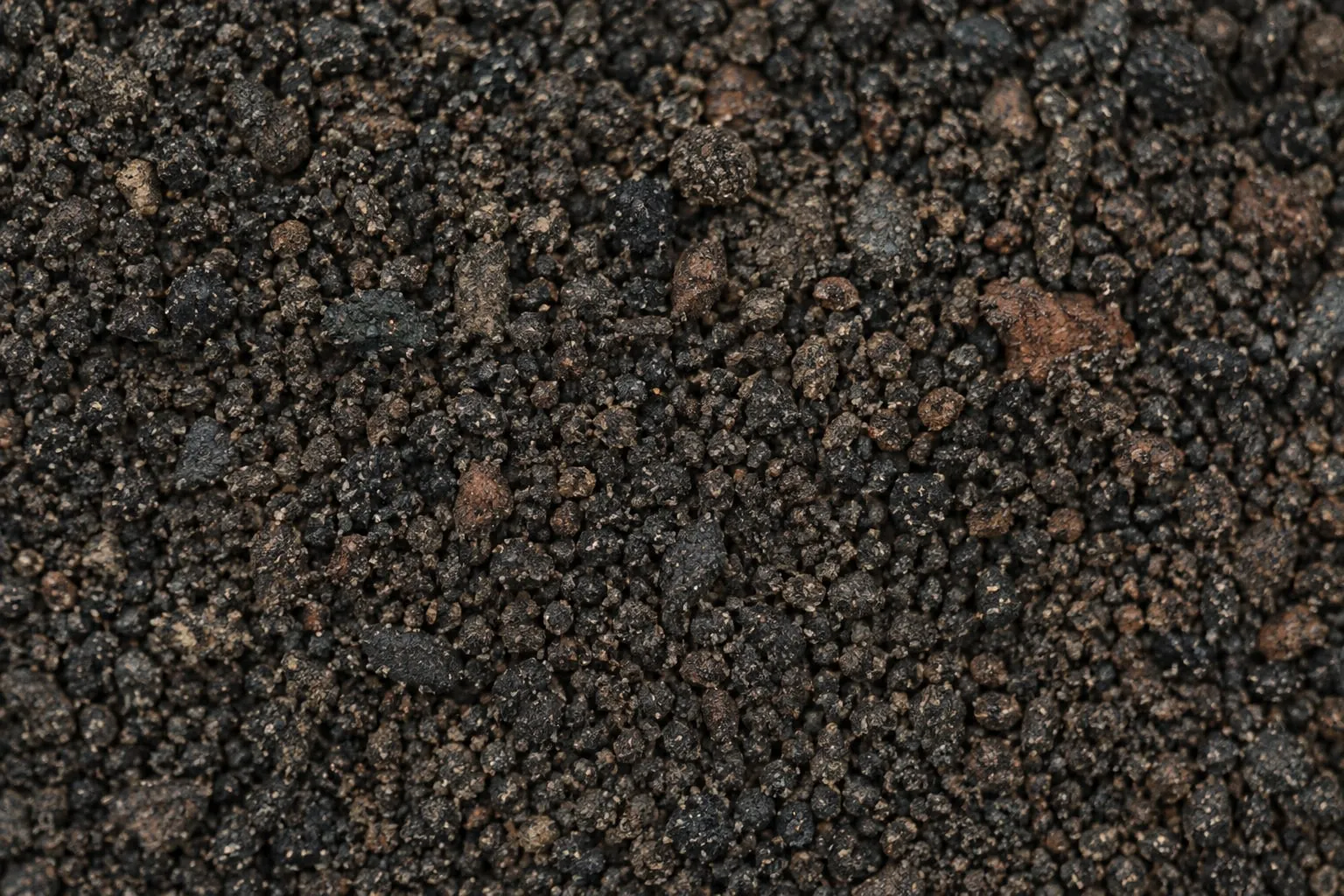 Illustrative visualisation: a close view of screened granular mineral material, dark grey and rust-brown particles of roughly even size filling the frame